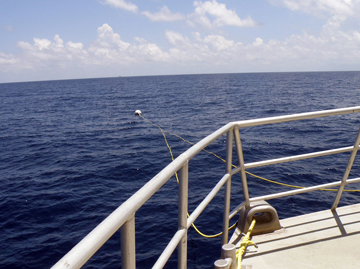 Looking past the front railing of a boat to the mooring buoy floating on the surface of the ocean.