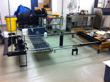 A metal frame and other mechanical parts laid out on a worksroom floor for assembly.