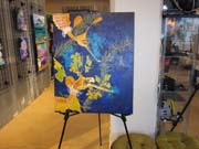 A large painting of two weedy seadragons on a bright blue background.  The painting is standing on an easel.