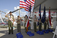 One Boy Scout holds the American flag aloft while the other scouts dip the Texas, NOAA, Sanctuaries, and Troop flags dipped in salute.  Two scouts salute the flag with their hands to their brows.