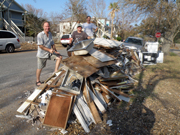 Three people stand alongside a debris pile in front of a Galveston home