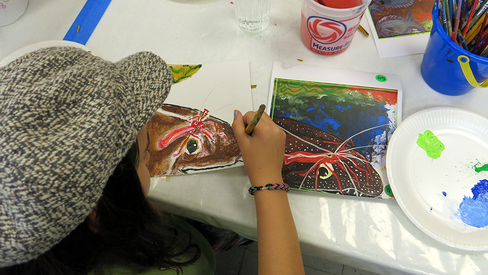A child painting a picture of an eel with a shrimp sitting on its head
