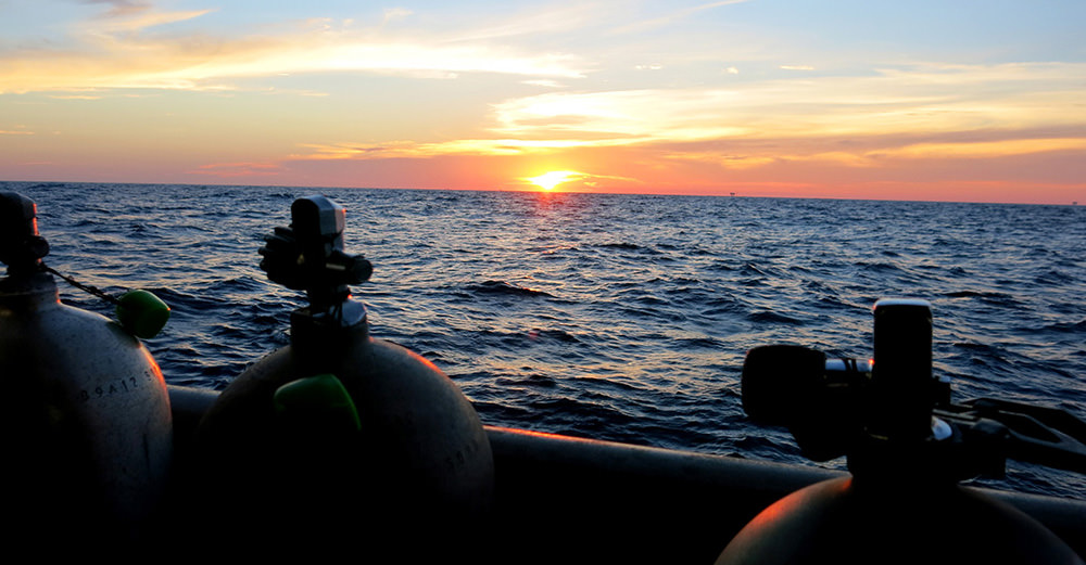 The tops of 3 scuba tanks silhouetted against an ocean sunset