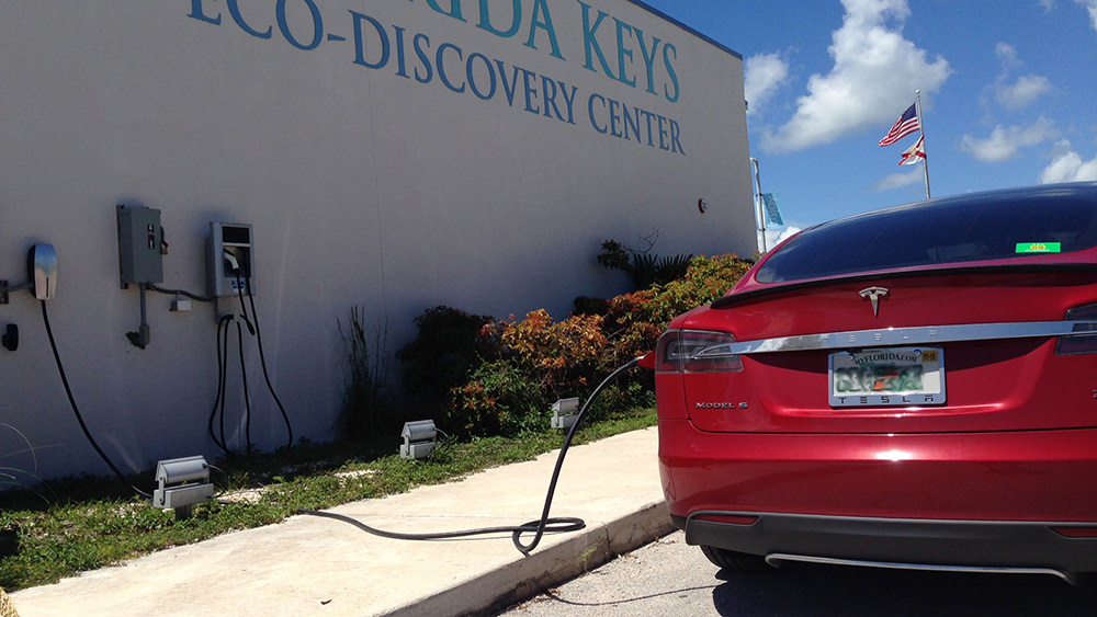 A red car plugged into a charging station on the side of a building