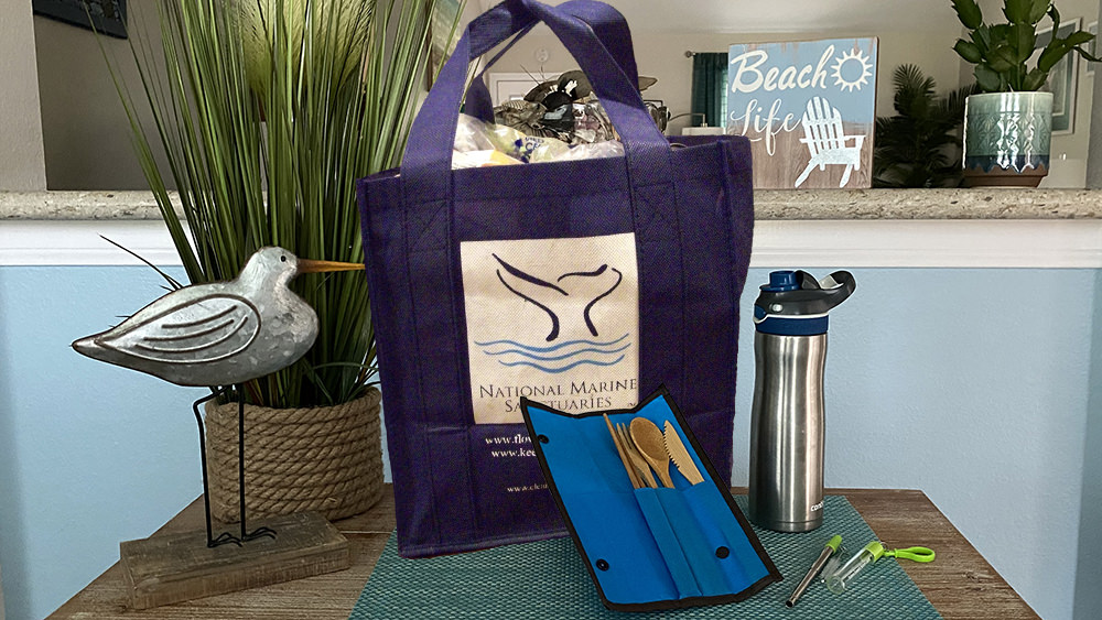 A reusable shopping bag, a water bottle, a set of bamboo utensils, and a metal straw arranged on a table