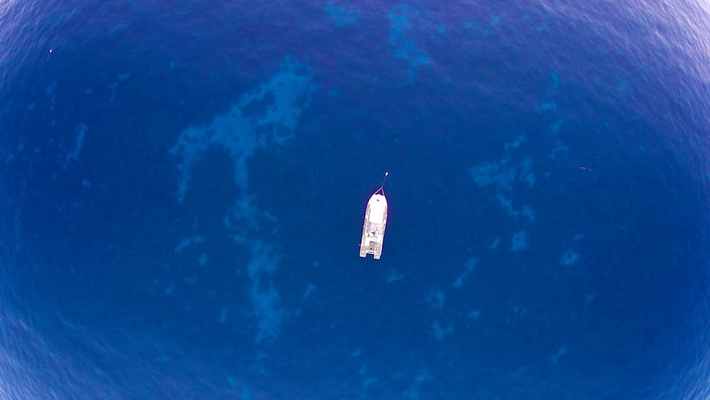Overhead view from hundreds of feet above the water showing R/V MANTA moored in the sanctuary and the reefs visible far below.